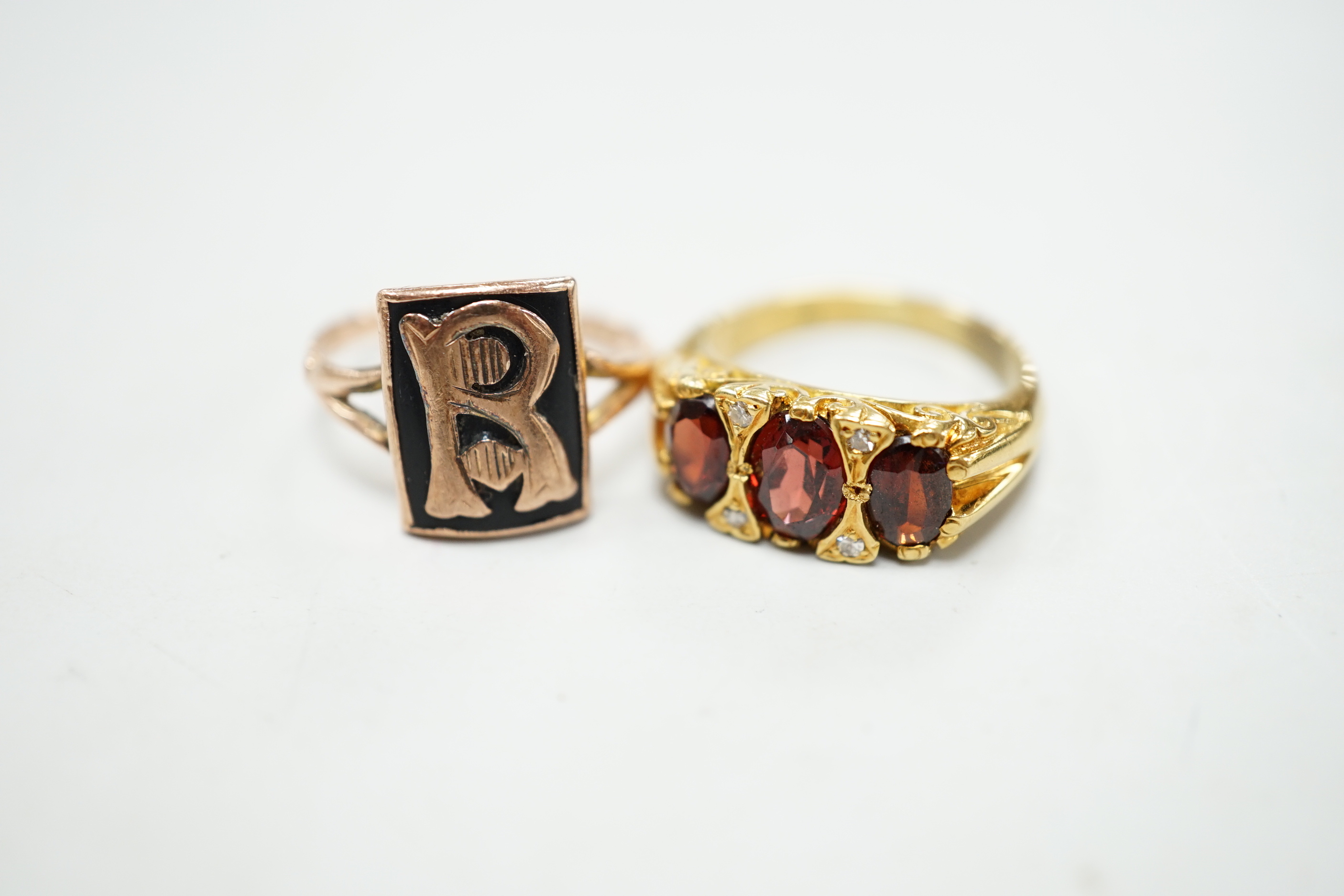 A yellow metal and three stone garnet set ring, with diamond chip spacers and a 9ct and black enamel set initial ring, gross weight 10.1 grams.